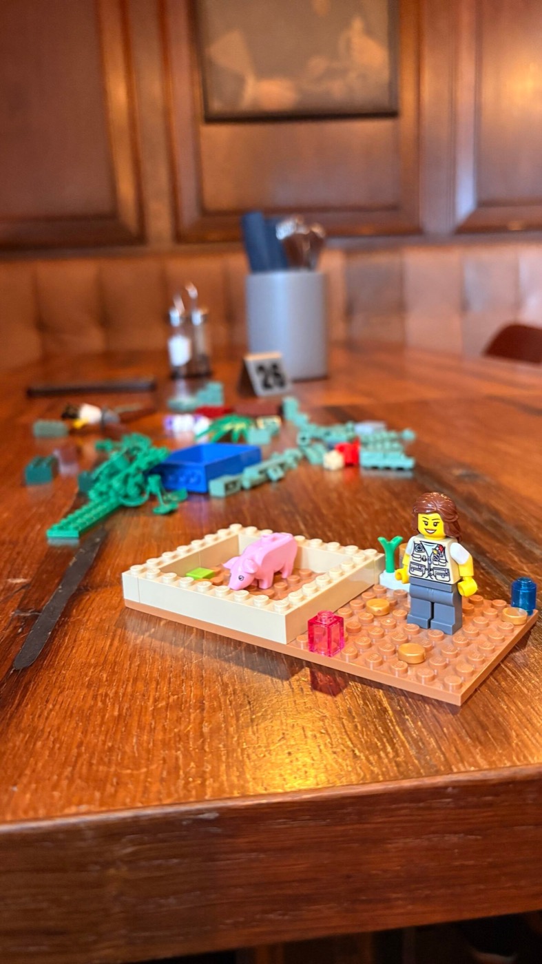 Lego-Stall mit rosa Schwein und Cowboy-Minifigur auf einem Holztisch