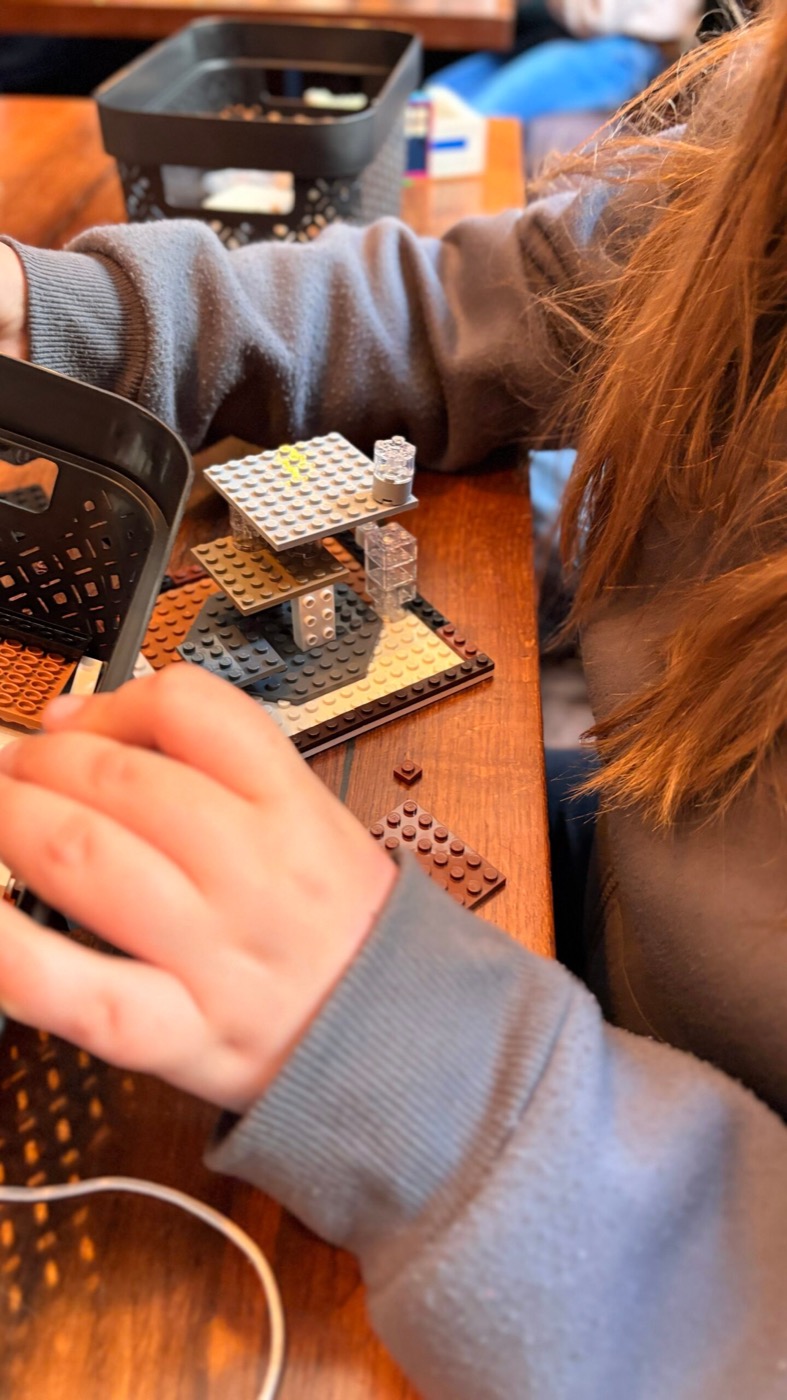 Hände eines Kindes bauen mit Lego, daneben ein schwarzer Sortierkorb