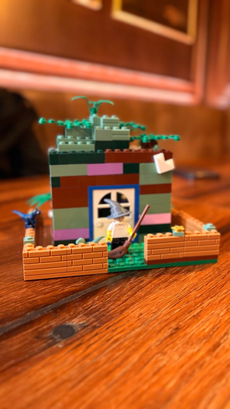 Fertiges Lego-Hexenhäuschen mit Hexen-Minifigur und Besen vor blauem Fenster