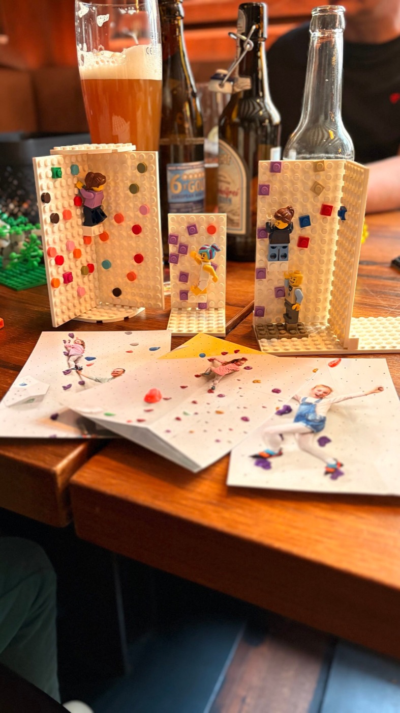 Lego-Kletterwand neben gemalten Kletter-Karten und Bierflaschen auf dem Tisch