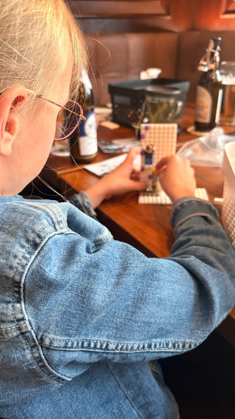 Mädchen mit Jeansjacke baut eine Lego-Minifigur an einem Holztisch