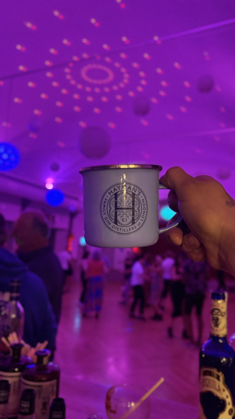 Eine Hand hebt einen Becher über die tanzende Menge bei der Fiesta Latina im violetten Licht