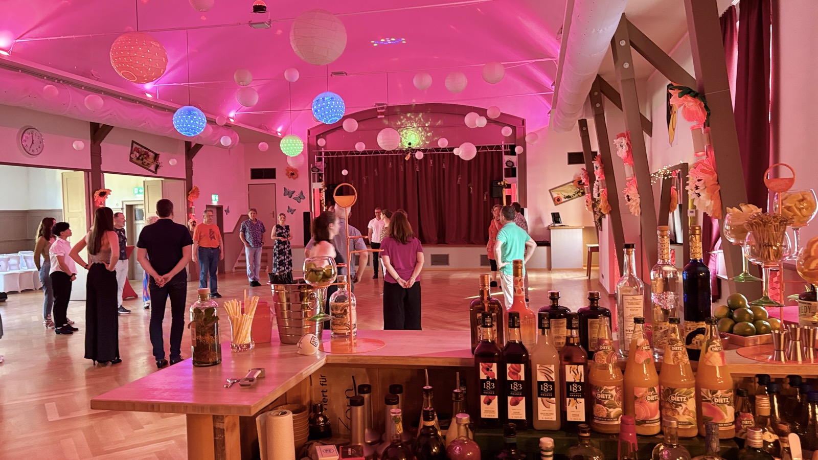 Der Ballsaal des TSC Schwarz-Gelb in pink-violettem Licht, mit Discokugeln, Papierlampions und der Bar von Casa Blumen im Vordergrund