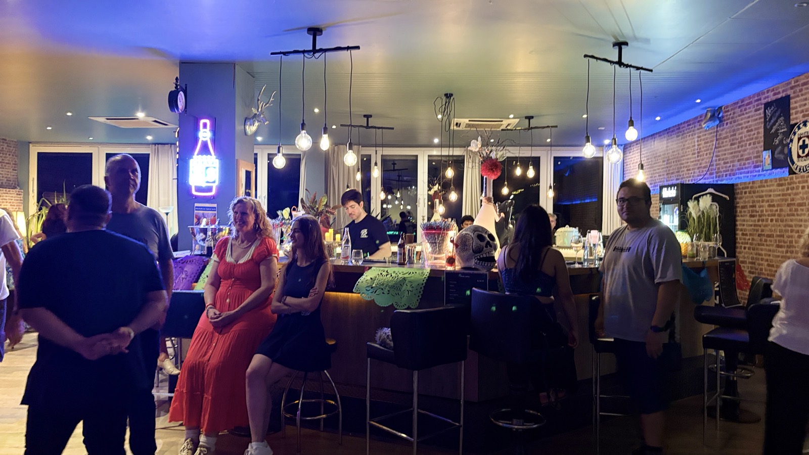 Gäste rund um die Casa-Blumen-Bar bei der Noche Latina im blauen Abendlicht, Backsteinwand im Hintergrund