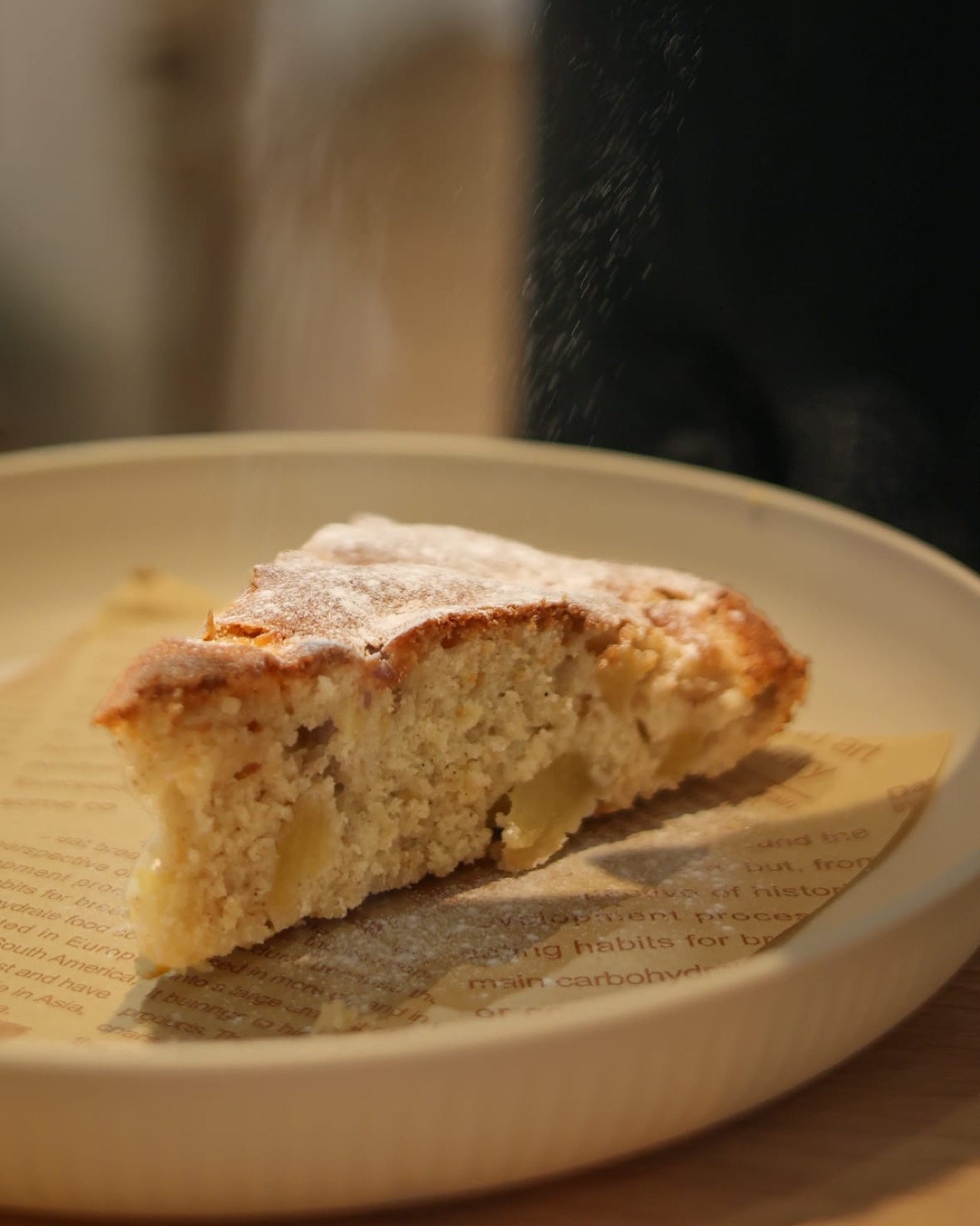Ein Stück Apfelkuchen mit fallendem Puderzucker