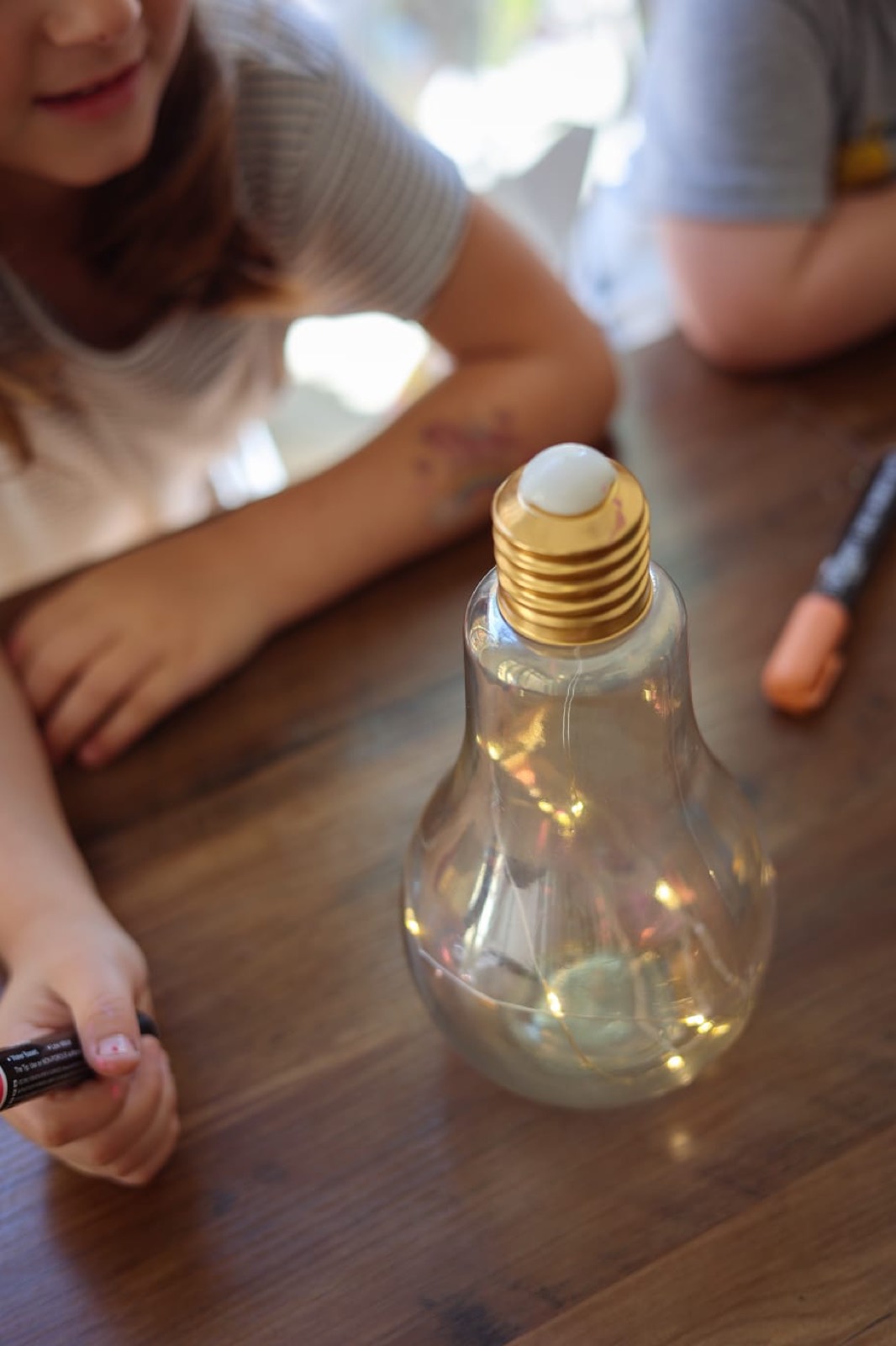Glühbirnen-Flasche mit Lichterkette auf einem Holztisch, Kinder ringsherum