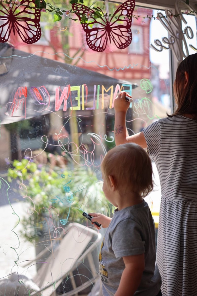 Kinder bemalen die große Fensterscheibe des Cafés mit bunten Stiften