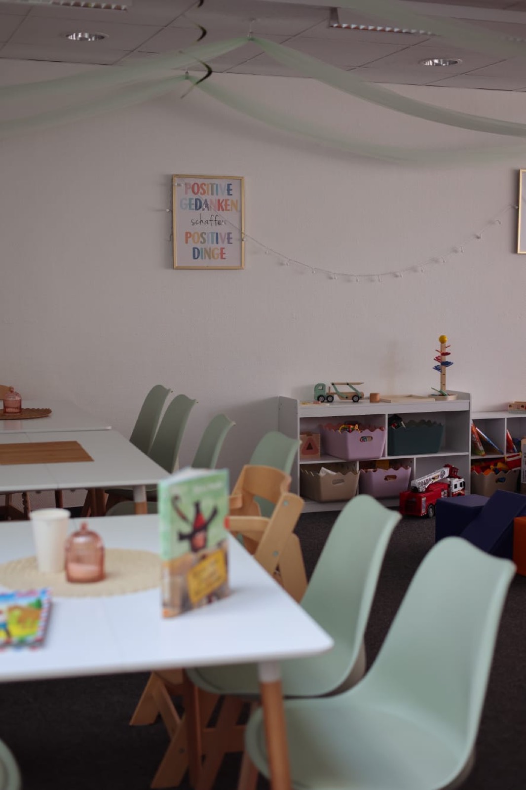 Tische und mintgrüne Stühle unter Girlanden im Obergeschoss des Goldkrümel