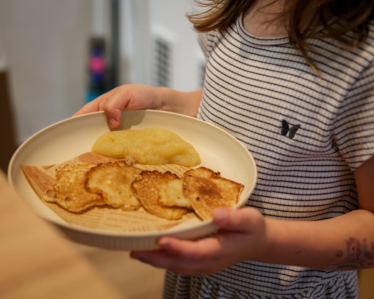 Kind hält einen Teller mit kleinen Pfannkuchen und Apfelmus